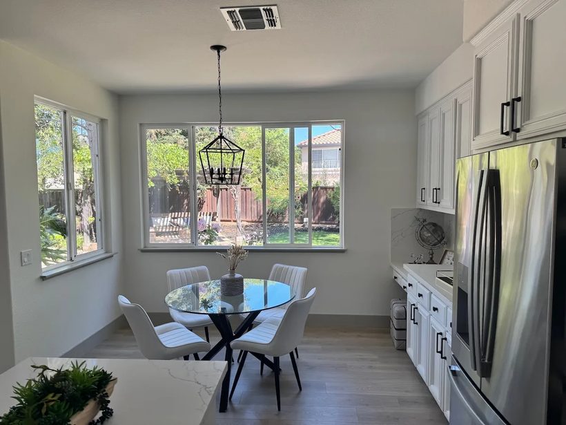 A kitchen dining nook with white chairs around a glass table